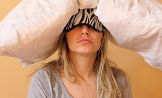 Frau mit Schlafmaske und einem Kopfkissen auf dem Kopf